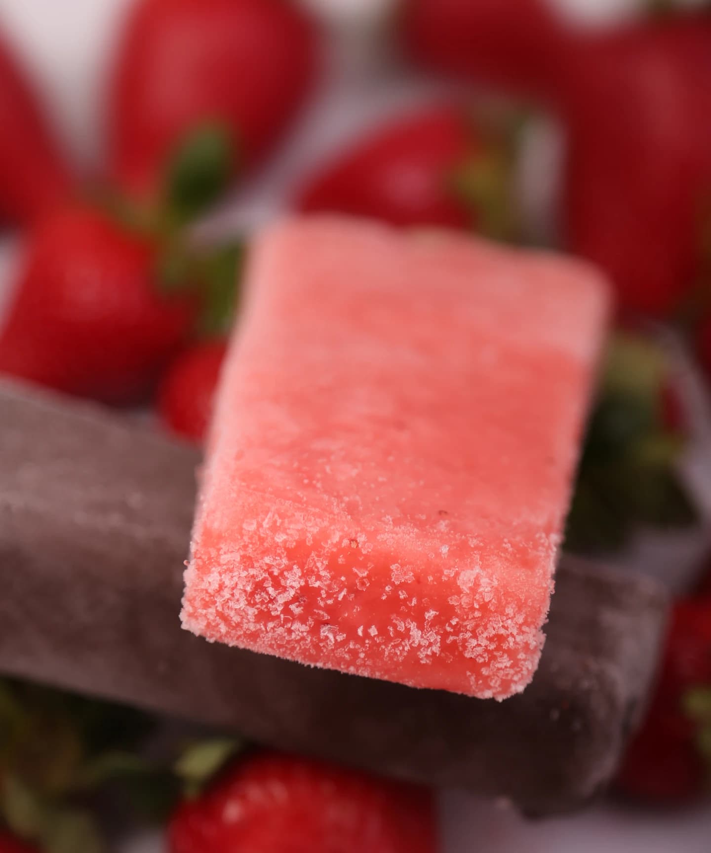 A woman in a frayed white bucket hat biting into a chocolate-striped ice lolly in hard sunlight.